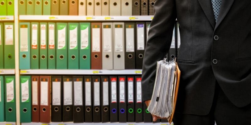 Male attorney holding thick case file in front of shelf of legal files and paperwork