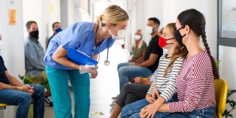 Female nurse speaking with mother and child in medical office waiting room