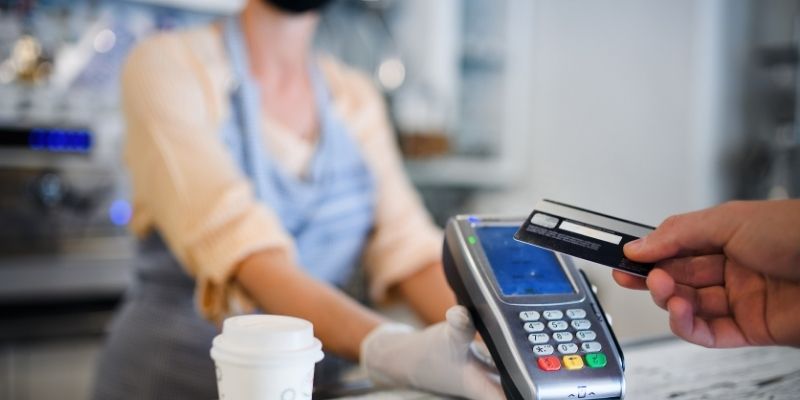 Female cafe owner wearing mask collecting payment by credit card