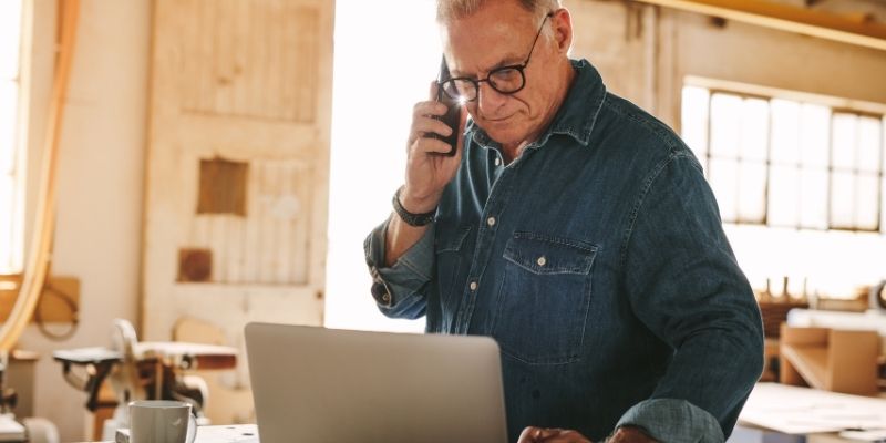 Older male small business owner on the phone looking at laptop