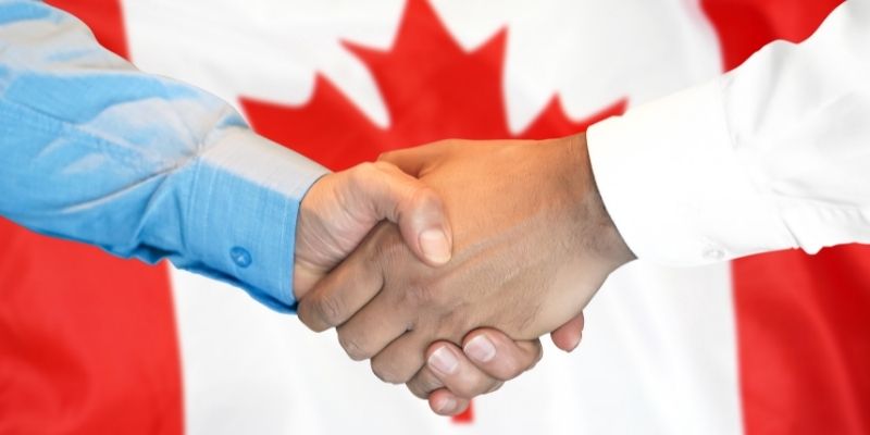 hands shaking in front of waving canadian flag